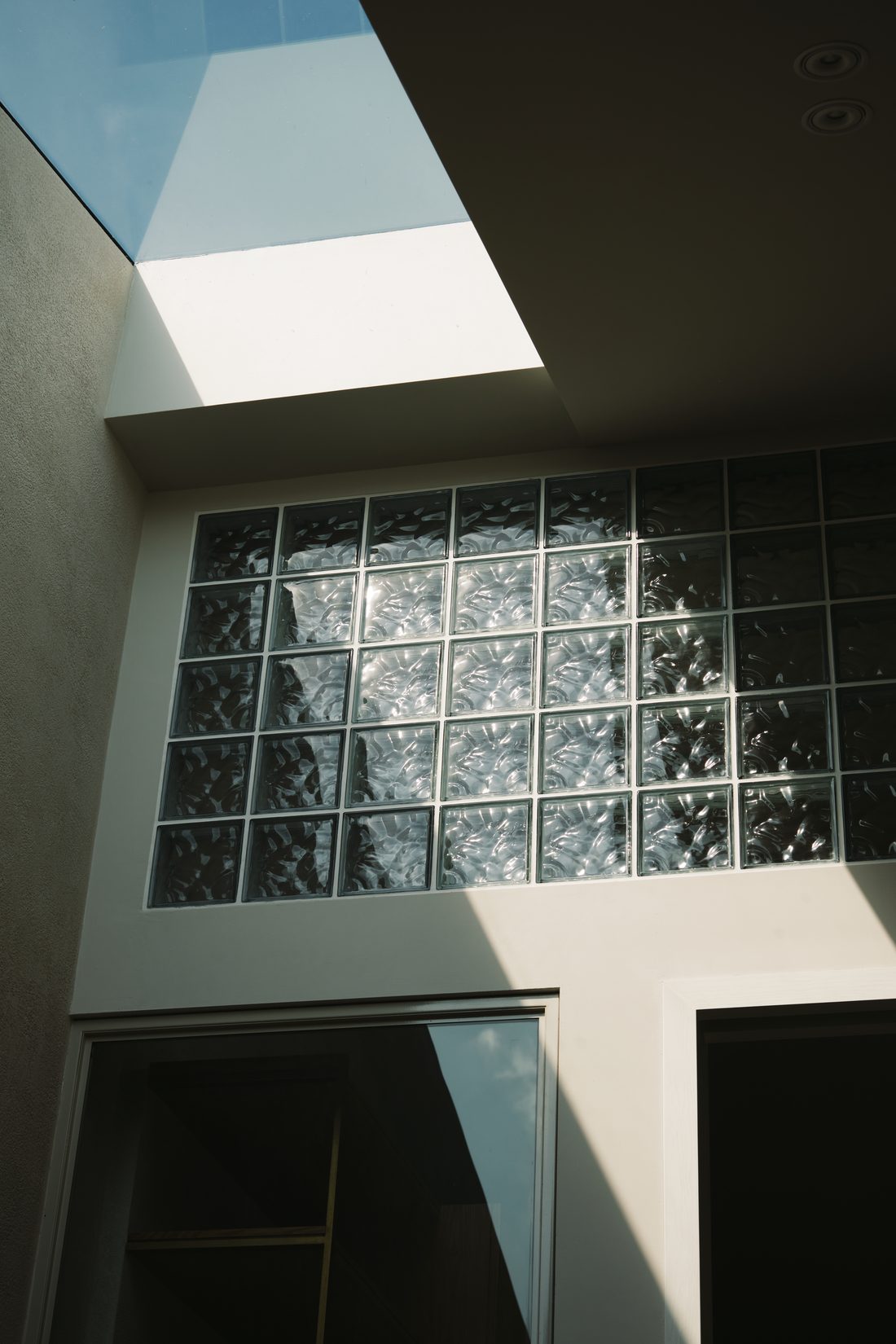 A wall of glass block rising into the skylight well, catching the afternoon