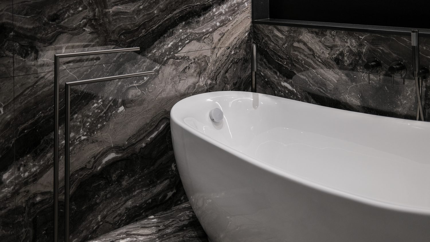 The master bath — a white freestanding tub against book-matched dark marble