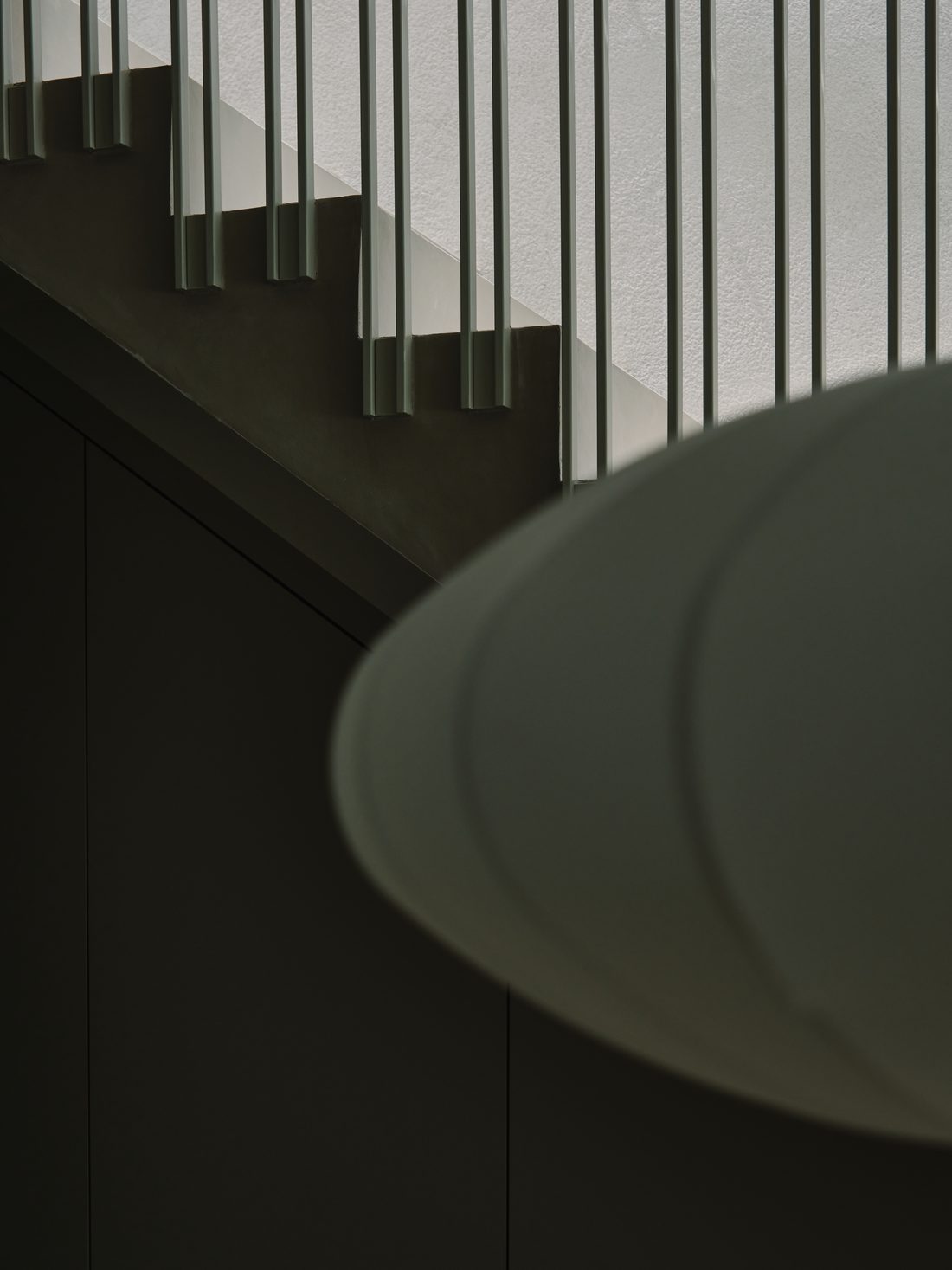 A close view of the stair — metal rods and the curve of a Nelson saucer lamp