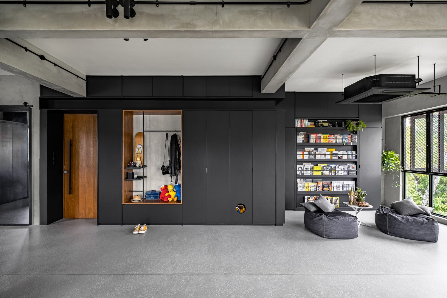 An industrial loft — a black storage wall with a warm timber niche, beanbags on polished concrete
