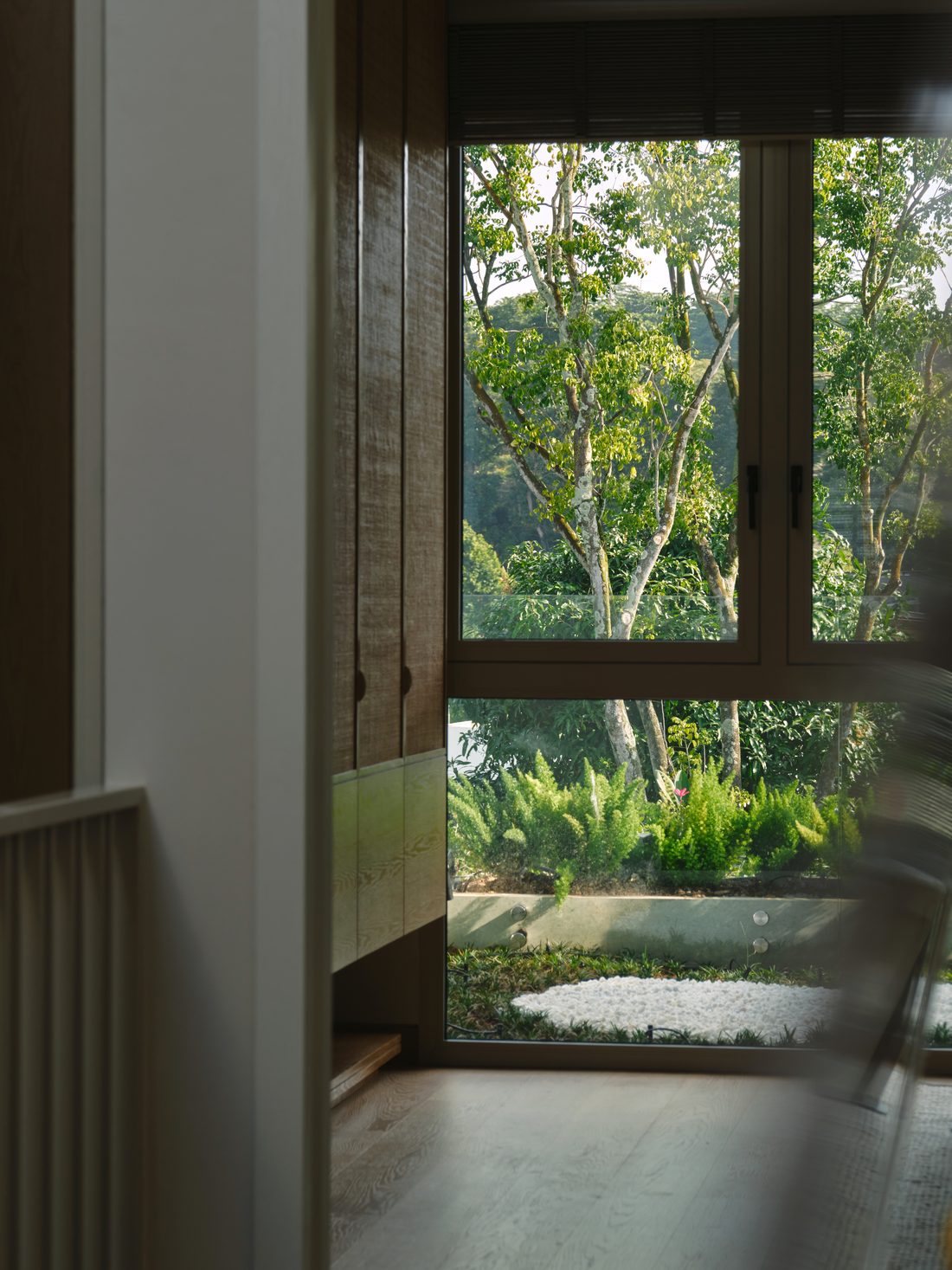 A bedroom window framing the rainforest canopy, oak floor and rattan joinery