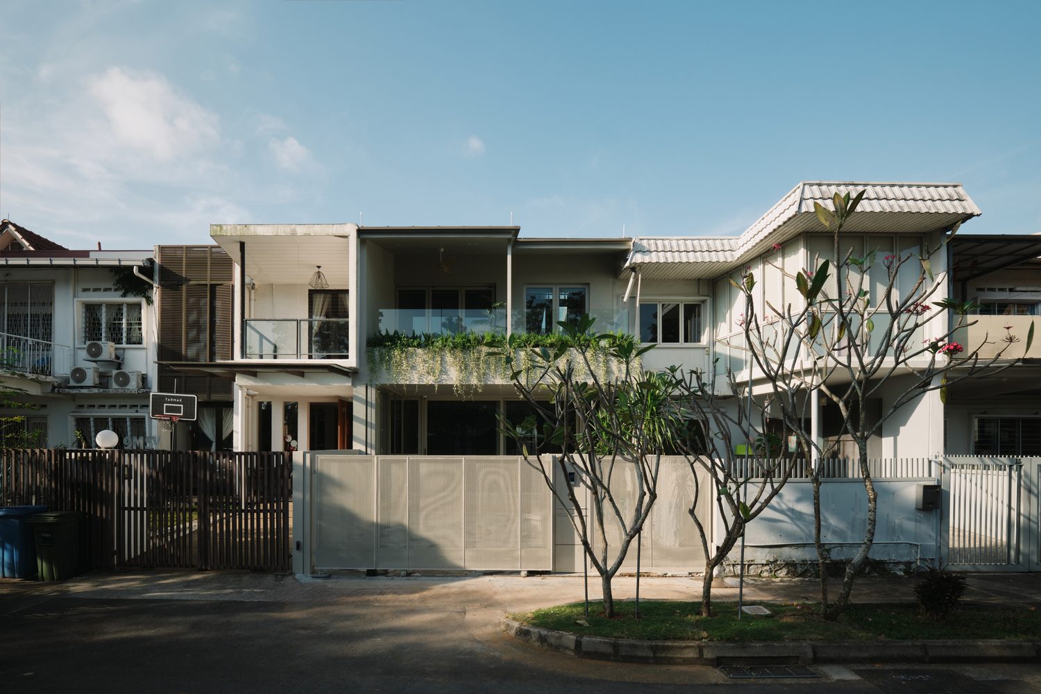 The street elevation — a white terrace house behind a perforated metal gate, framed by frangipani