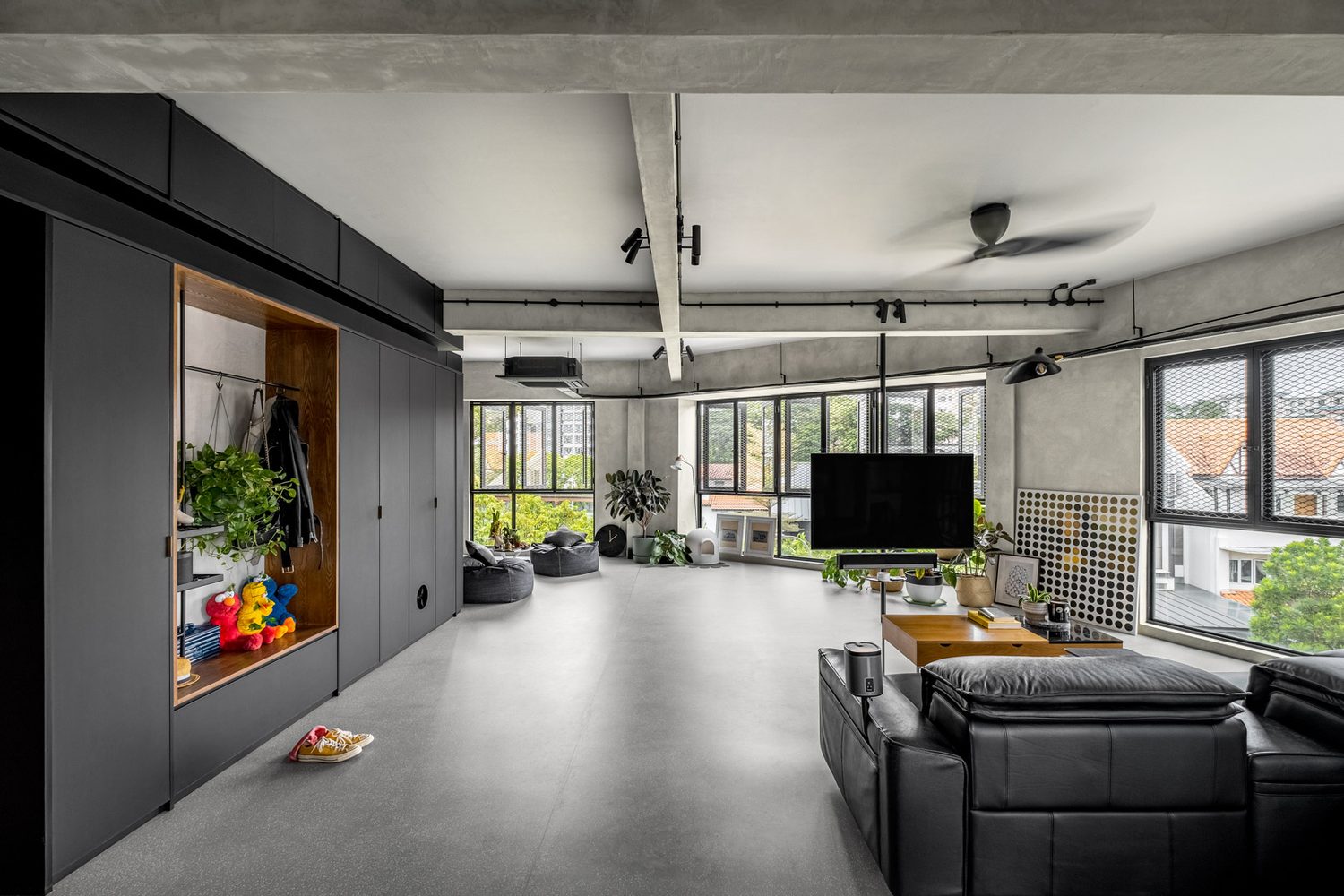 The living area — a black leather sofa below mesh-screened windows, concrete throughout