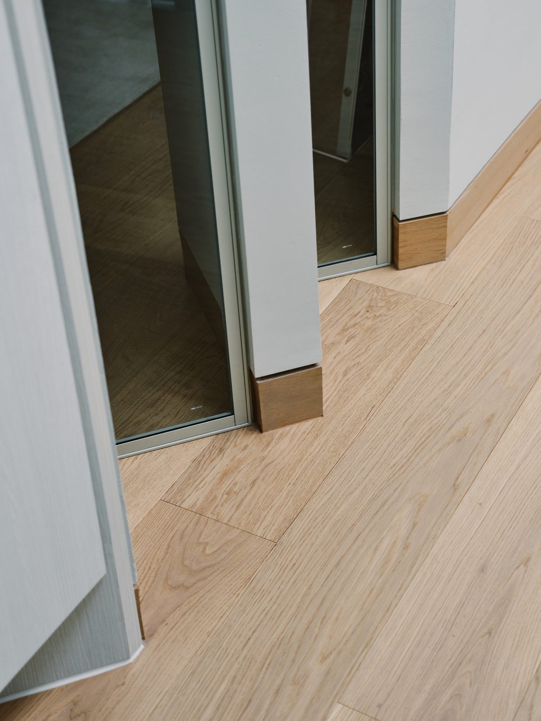 A detail — oak flooring meeting slim glazed pivot doors at the threshold