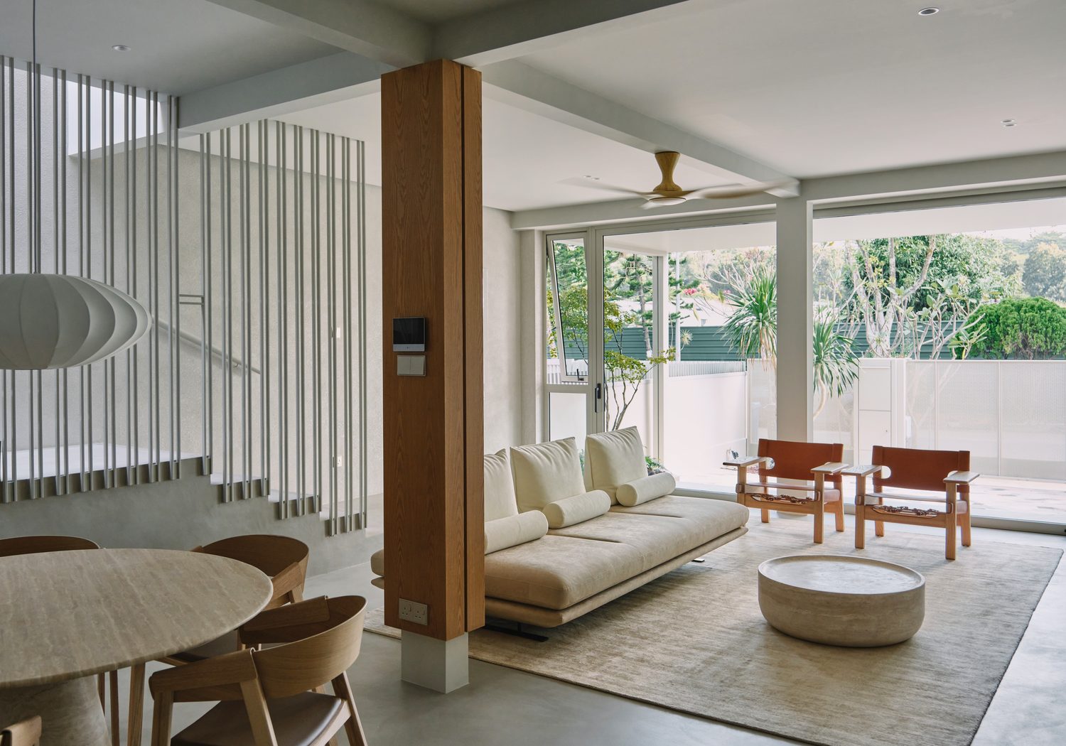 The living room — a pale sofa and leather sling chairs opening to the garden through full-height glass