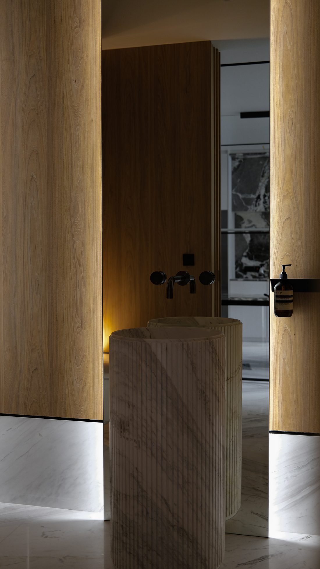 A powder room — a fluted marble pedestal basin between warm timber walls