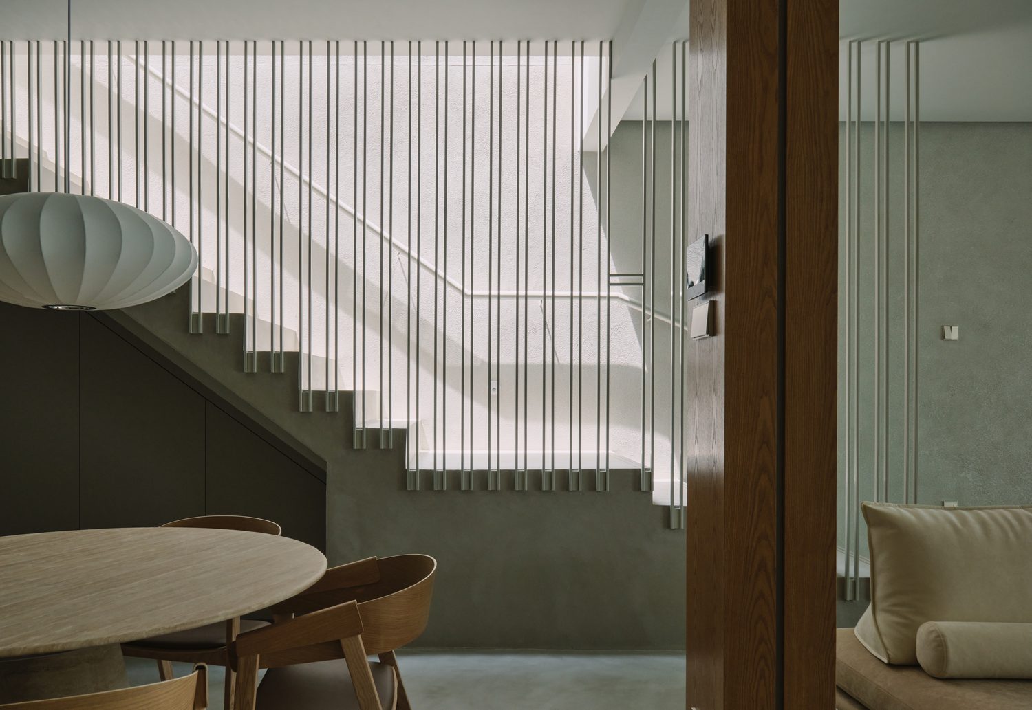 The stair hall — a slatted metal balustrade beside the round dining table and an oak column