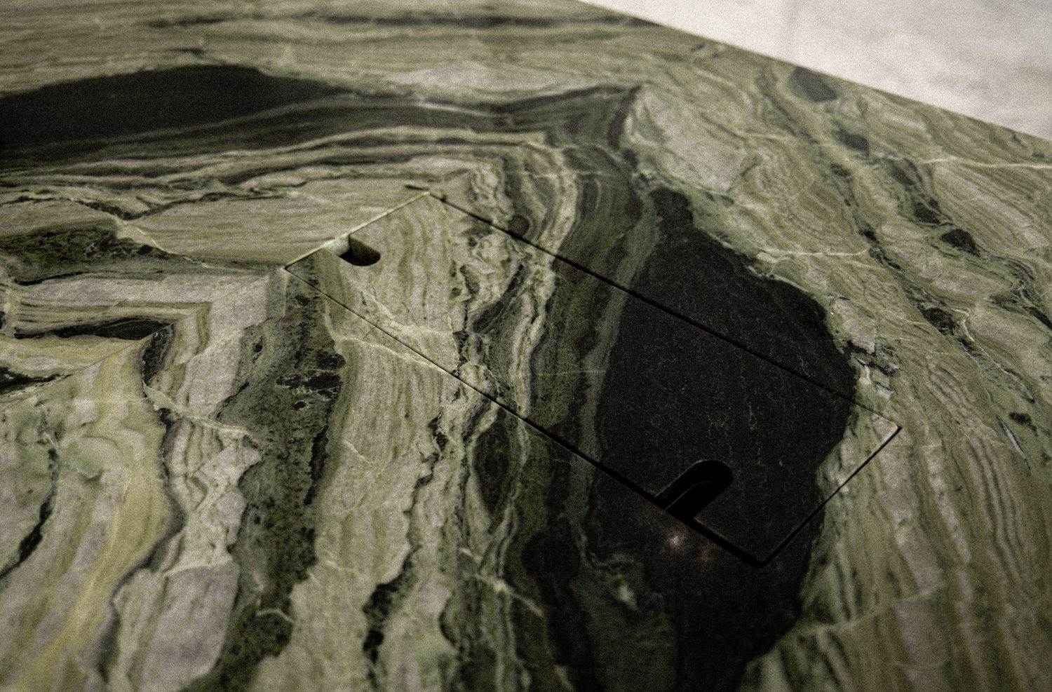 A detail — a recessed black tray notched into the green-marble worktop