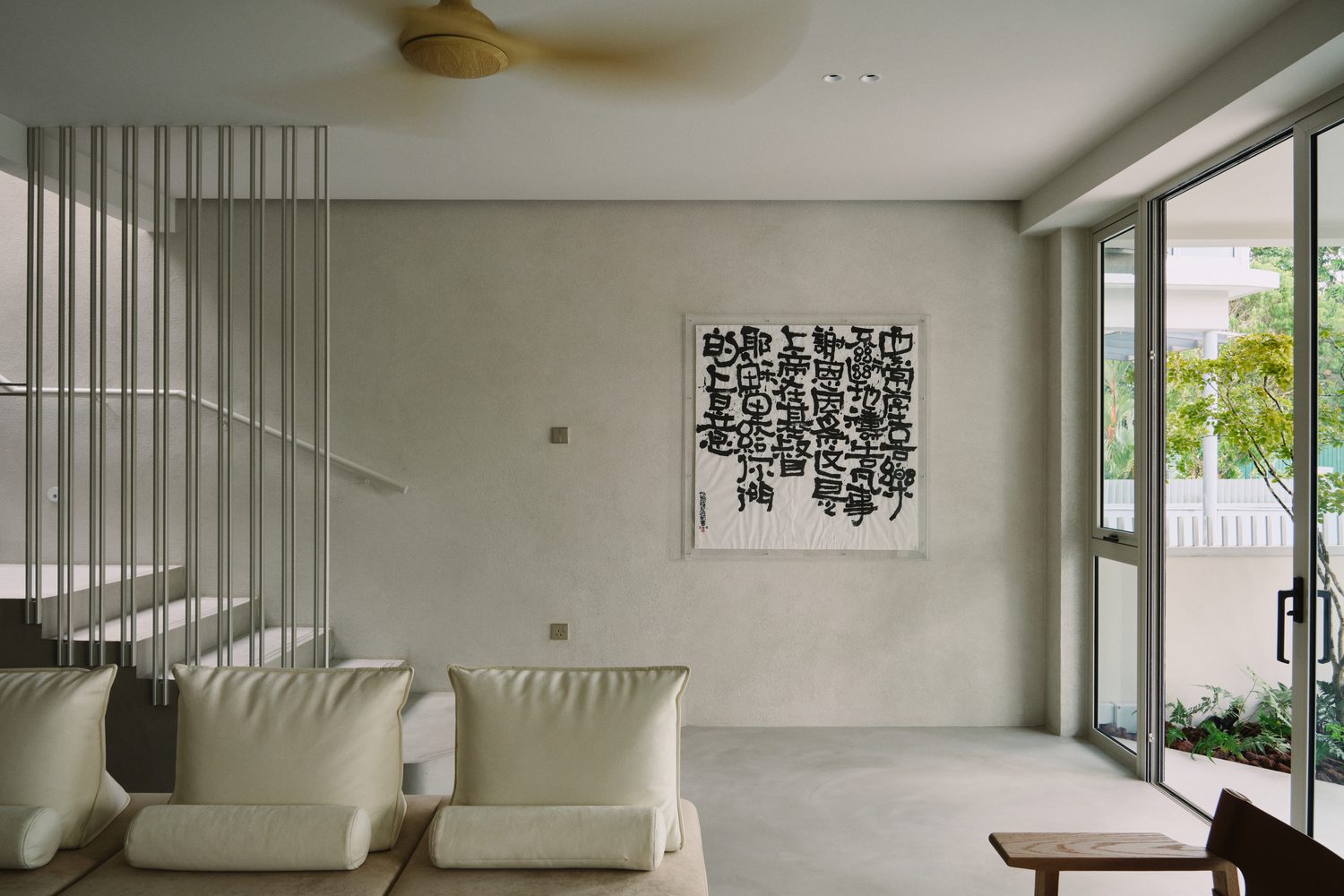 The living room — a low sofa beneath a large ink-calligraphy scroll, garden light from the right