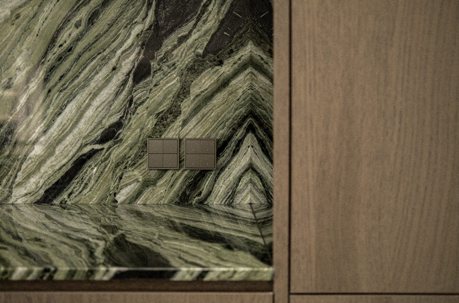 A detail — bronze switch plates set into book-matched green marble beside oak