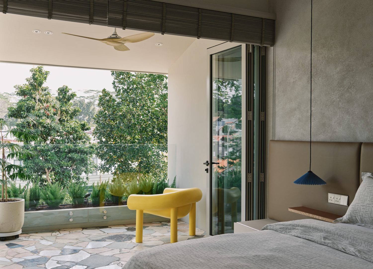A bedroom opening to a terrace of crazy-paved stone, a yellow tub chair at the glass