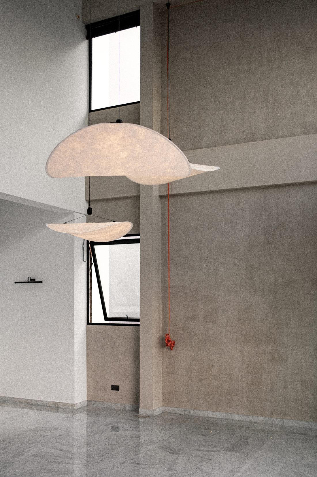 A double-height void — two suspended fabric pendants drifting against board-formed concrete