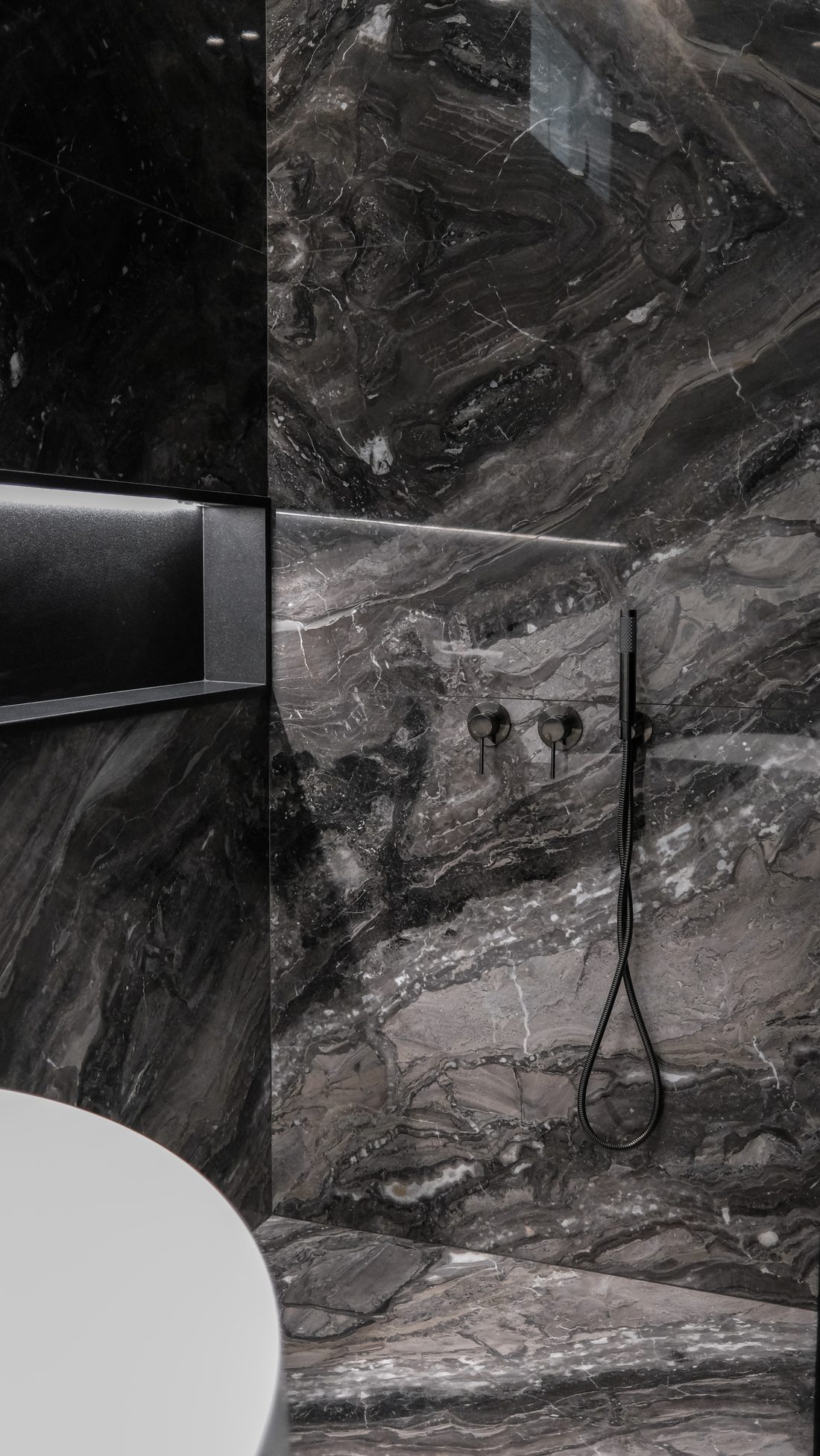 A shower wall of veined dark marble with a recessed niche
