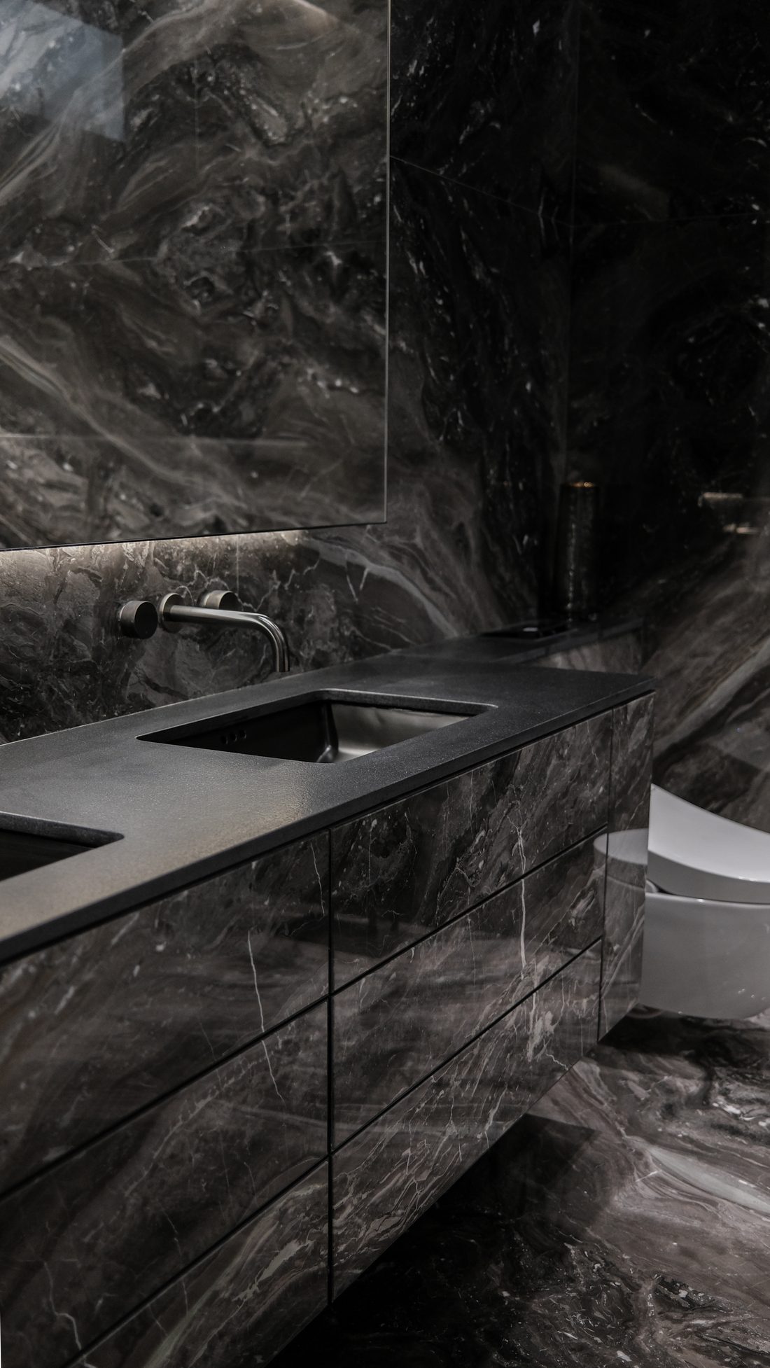A powder room in black marble — a honed basin and gunmetal tap