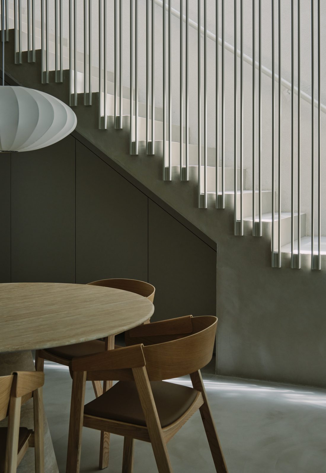 The cantilevered stair, its thin metal rods rising past the dining table