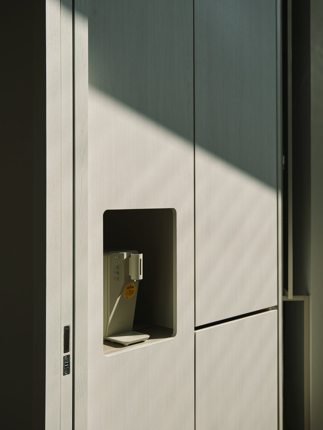 A detail — a recessed water tap set into pale oak joinery, raked by sun