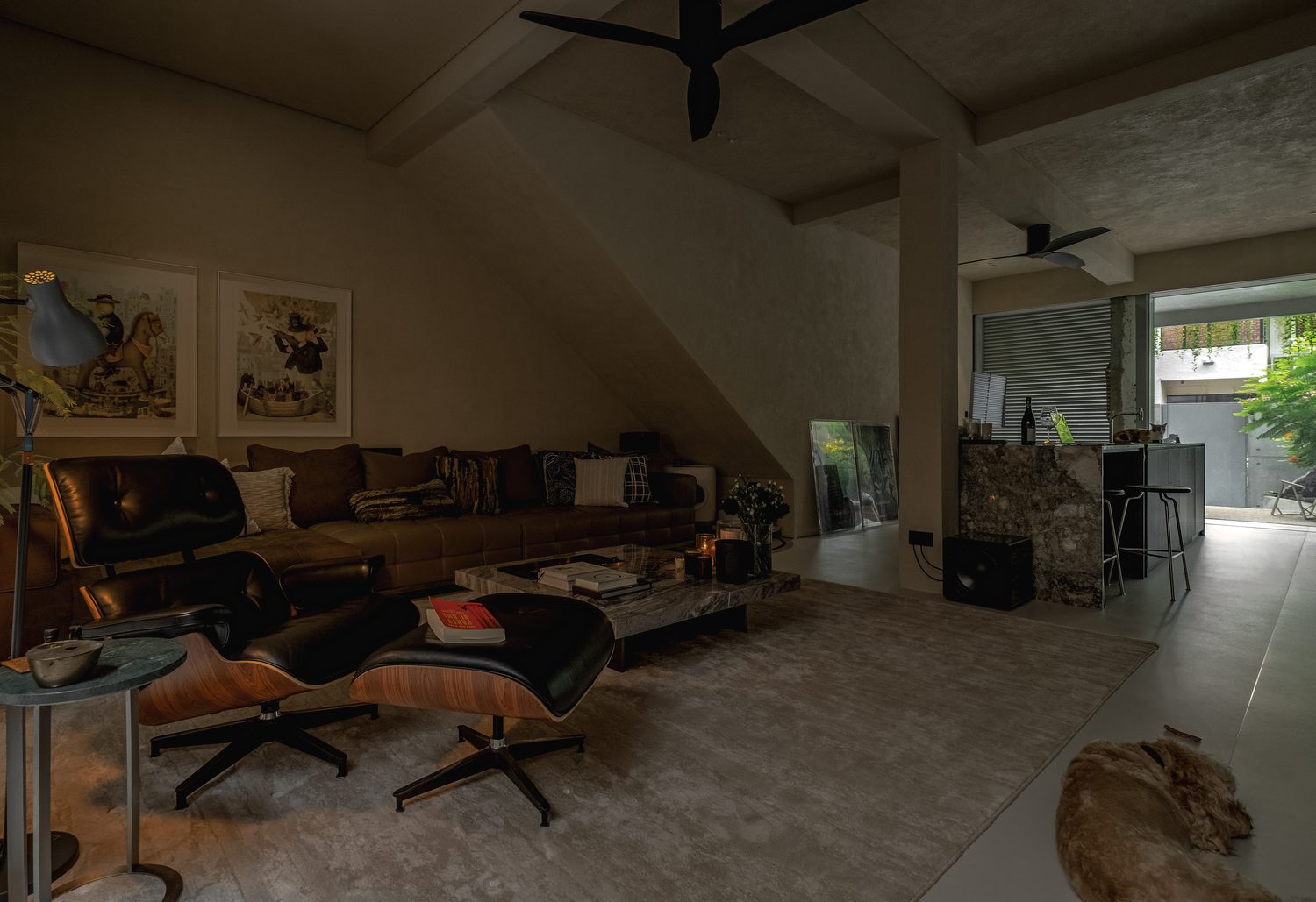 The living room by lamplight — a leather lounge chair, marble table and long sofa