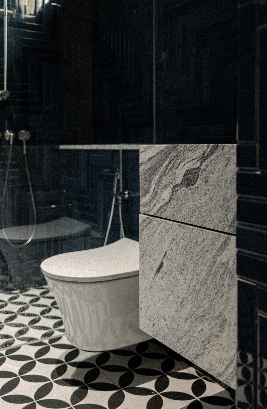 A powder room — a patterned tile floor, granite partition and a dark shower beyond