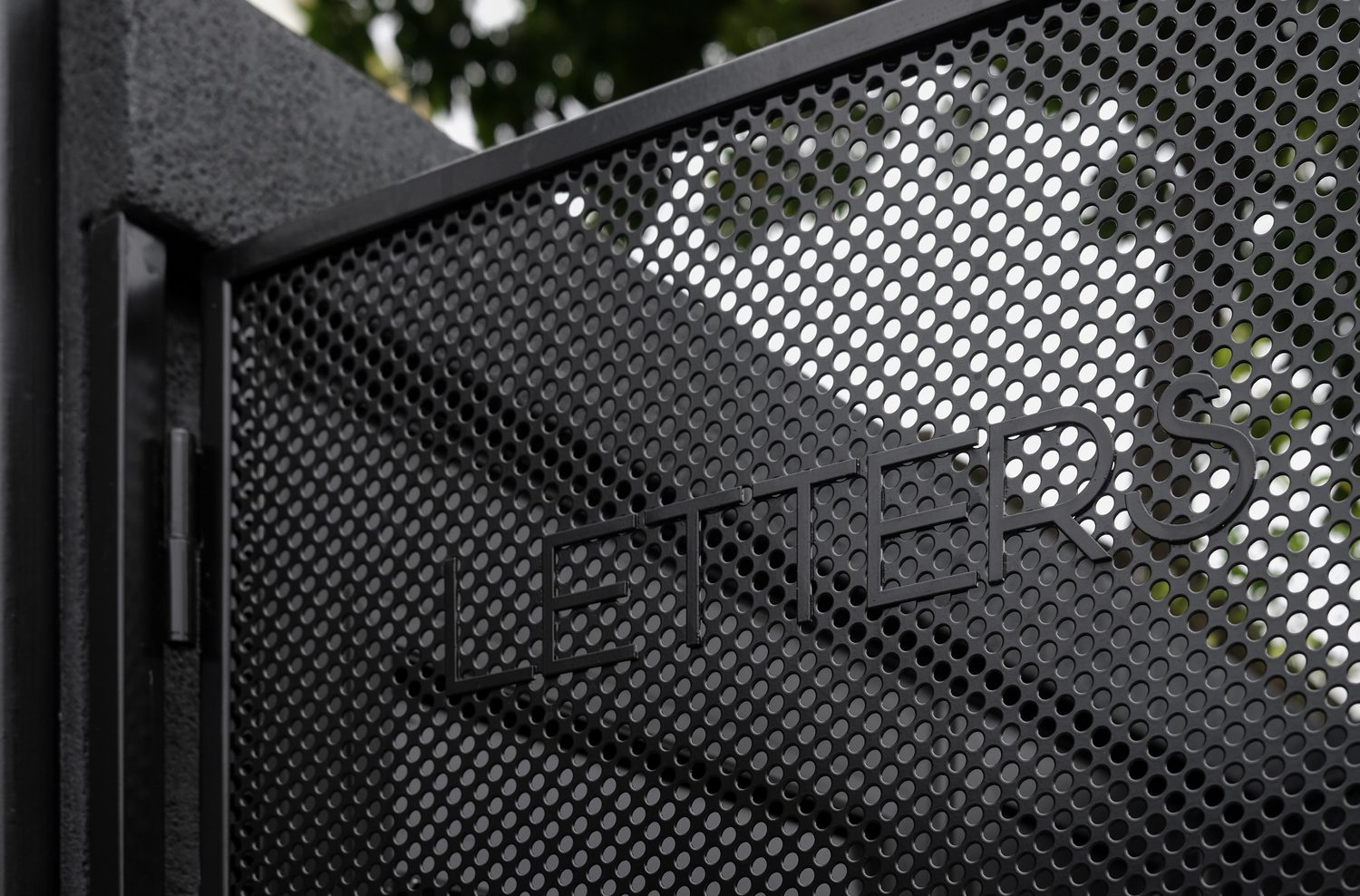 A detail — the letterbox, lettered into perforated steel